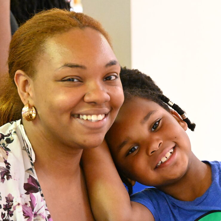 A mother and her young daughter smile cheek to cheek