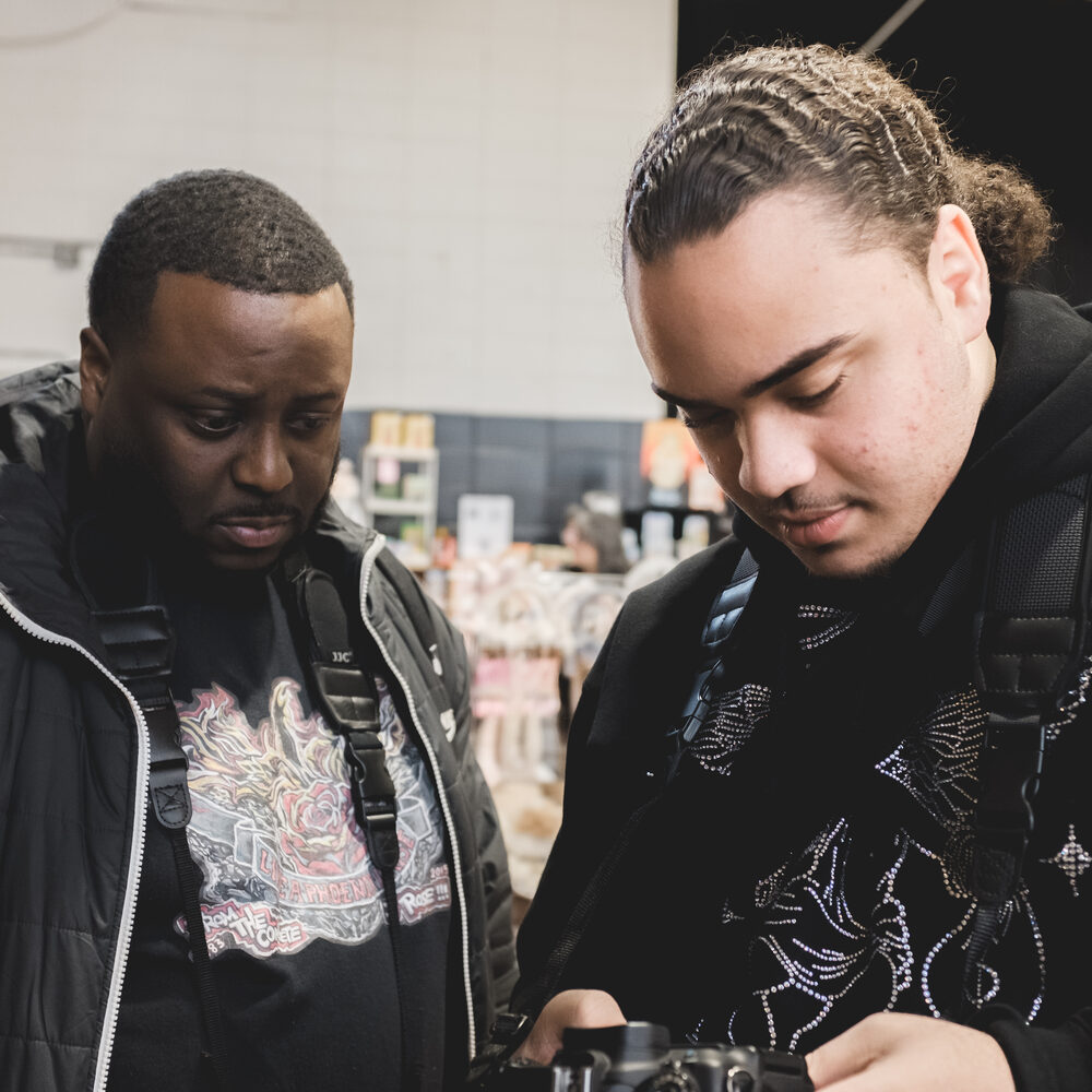 Mentor Tyese Williams and a teen look over a camera together
